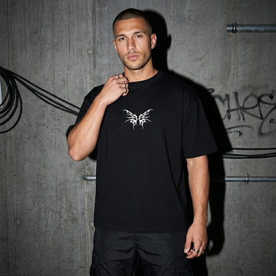 Schwarzes Tribal Techno Vibes Oversize T-Shirt, Vorderansicht am Model vor Betonwand #farbe_schwarz